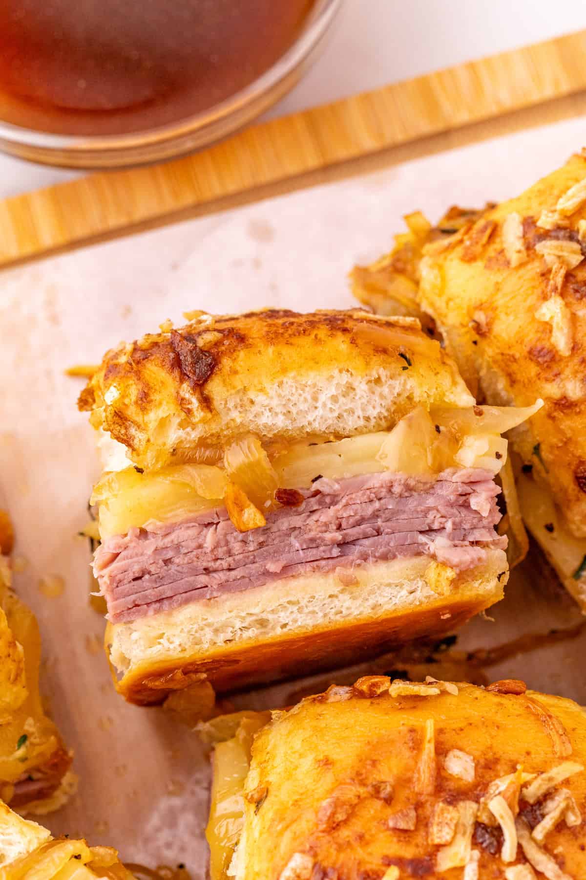 Roast beef, caramelized onions, and Swiss cheese are layered on Hawaiian rolls to make these easy French Dip Sliders. Overhead view of a French dip slider on its side