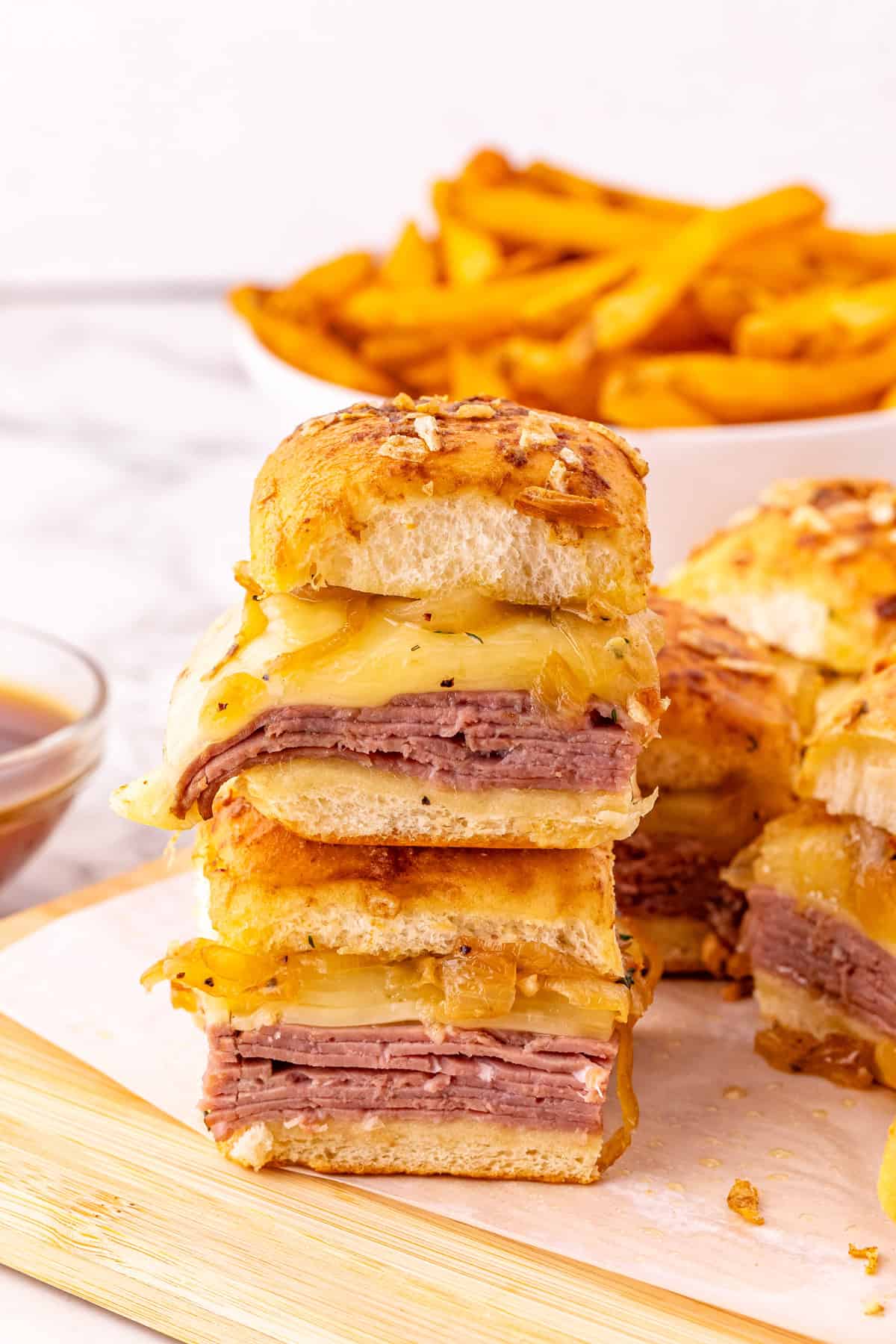 Roast beef, caramelized onions, and Swiss cheese are layered on Hawaiian rolls to make these easy French Dip Sliders. Two French dip sliders stacked on each other