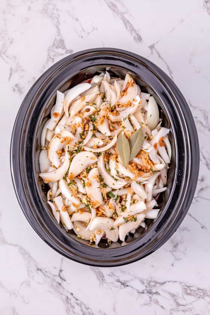 Seared chuck roast is slow cooked in savory broth and onion soup mix until fall-apart tender in this Slow Cooker French Onion Pot Roast. Sliced onions on top of a pot roast