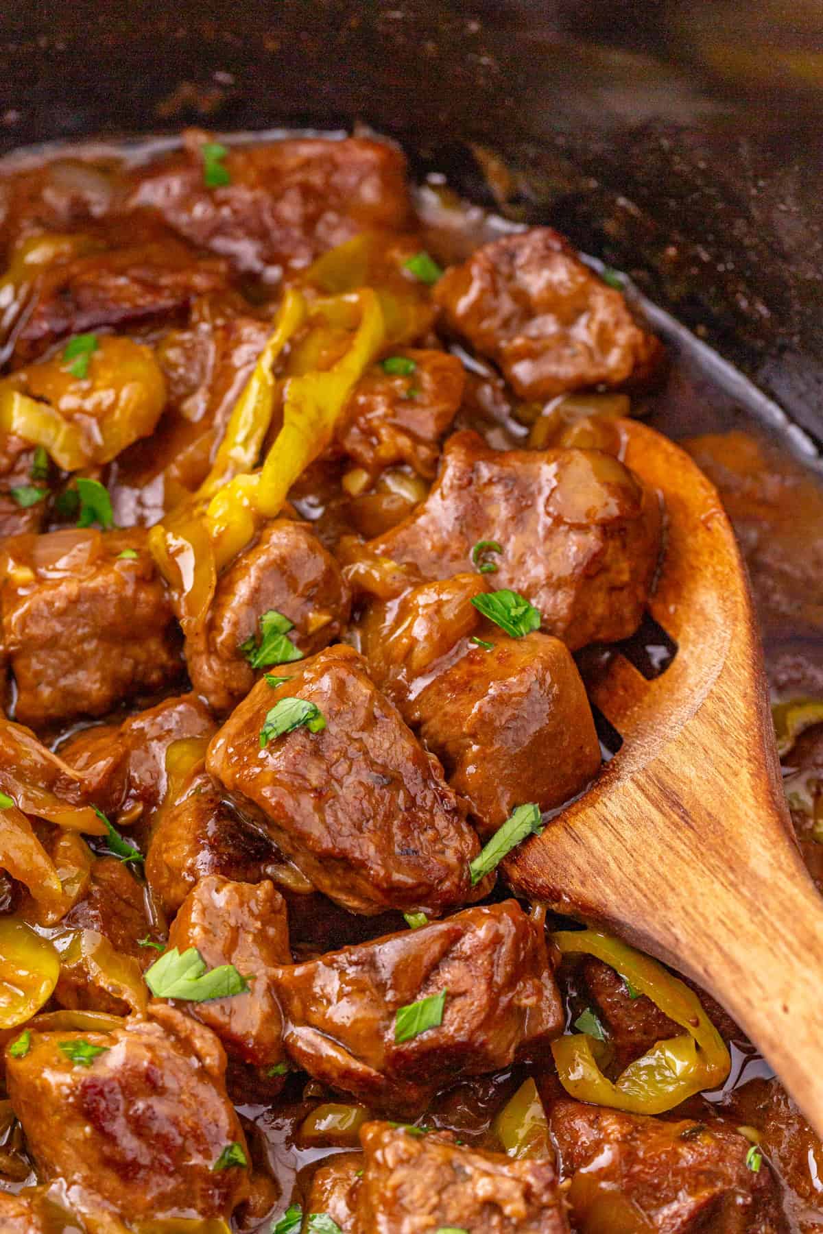 These Mississippi Steak Bites are savory, tangy, and so tender, with chunks of sirloin with ranch seasoning, au jus gravy, and pepperoncini. A wooden spoon stirring Mississippi steak bites
