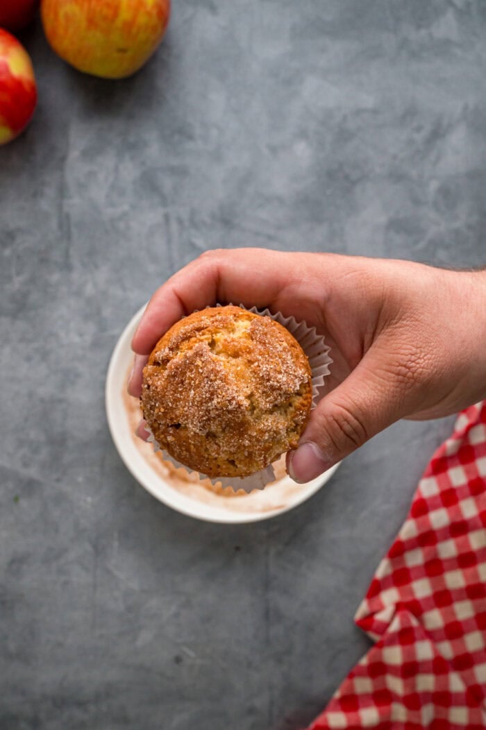 Each bite of these Applesauce Muffins is incredibly moist and infused with warm apple flavor. They look like something straight from a bakery! A hand holding aapplesauce muffin