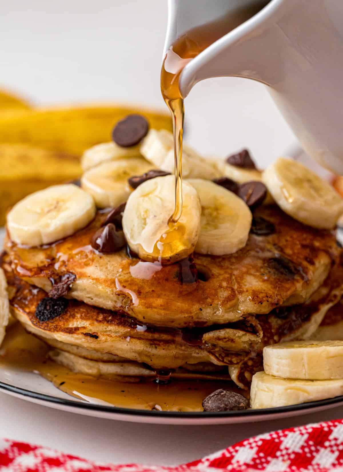 Every bite of these Banana Chocolate Chip Pancakes is dotted with chocolate chips and filled with sweet banana flavor. Stack of Banana Chocolate Chip Pancakes with maple syrup being poured on top