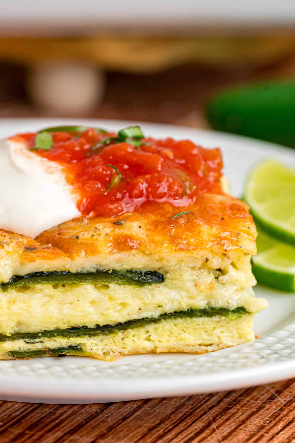 A slice of chile relleno casserole topped with sour cream and salsa on a white plate