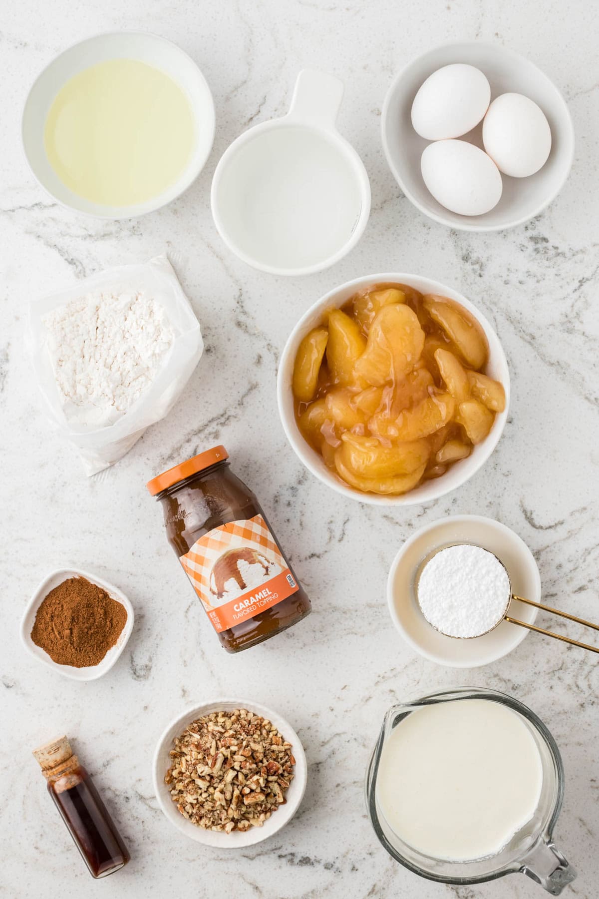 Vanilla cake is drizzled with caramel sauce and then topped with apple pie filling and whipped cream in this Caramel Apple Poke Cake recipe. Overhead view of ingredients needed to make caramel apple poke cake