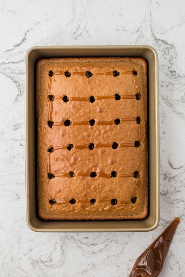 Vanilla cake is drizzled with caramel sauce and then topped with apple pie filling and whipped cream in this Caramel Apple Poke Cake recipe. A baked vanilla cake with holes poke in it