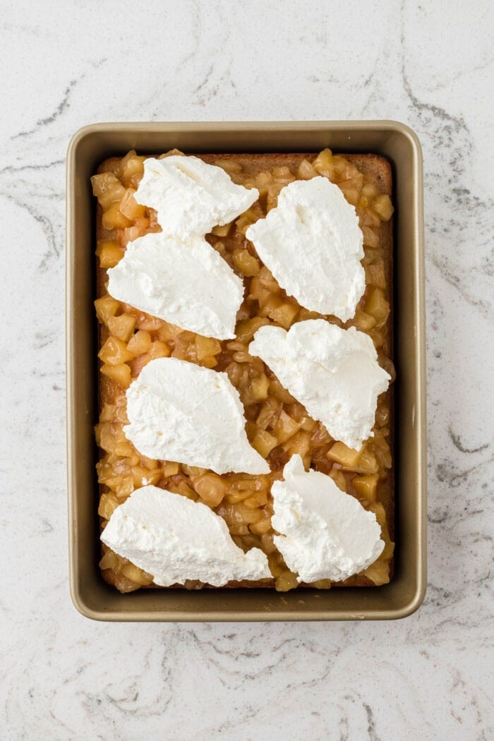 Vanilla cake is drizzled with caramel sauce and then topped with apple pie filling and whipped cream in this Caramel Apple Poke Cake recipe. Whipped cream on top of apple pie filling on a cake
