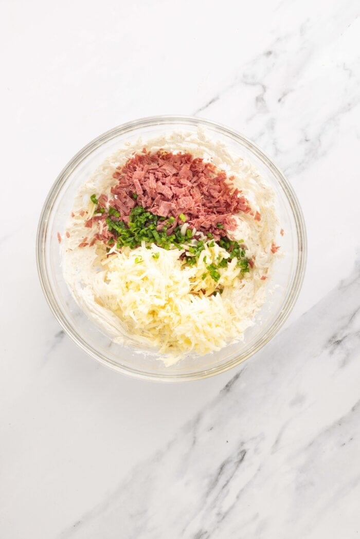 Salty dried beef combines with tangy cream cheese and sharp cheddar cheese to make this irresistible Chipped Beef Cheese Ball. Cream cheese, chipped beef, green onion, and cheddar cheese in a bowl