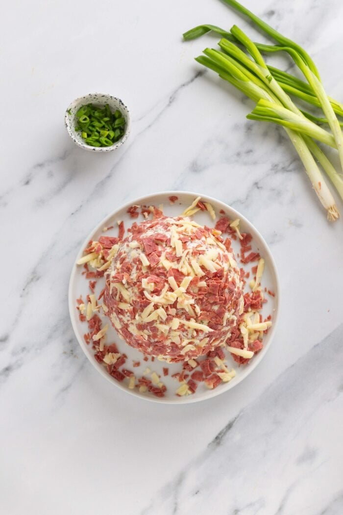 Salty dried beef combines with tangy cream cheese and sharp cheddar cheese to make this irresistible Chipped Beef Cheese Ball. Overhead view of a cheese ball coated in chipped beef and cheddar cheese