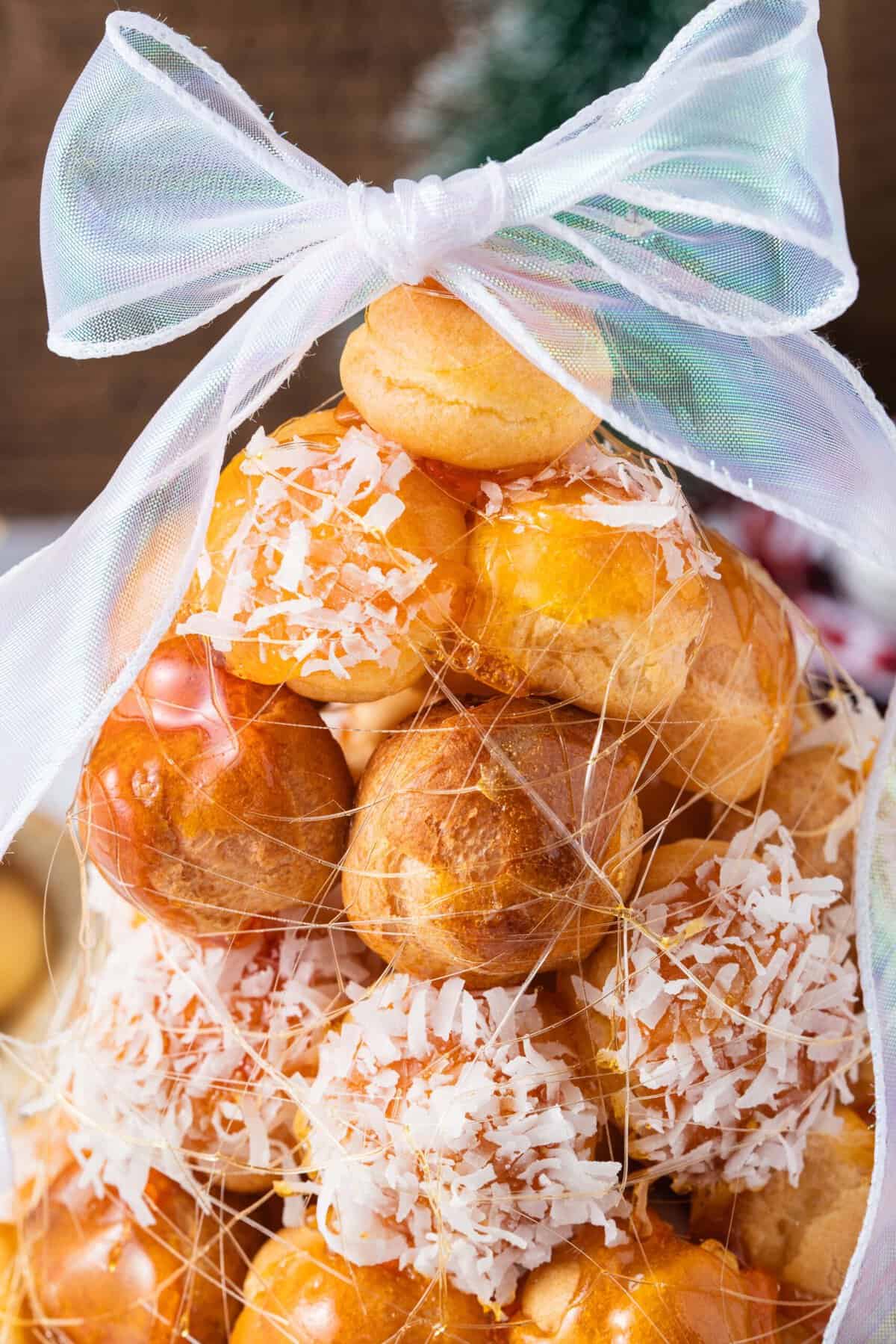 This festive Croquembouche features a stunning tower of cream puffs dipped in glossy amber caramel and sprinkled with shredded coconut. Close up of Croquembouche to show the brown sugar strands