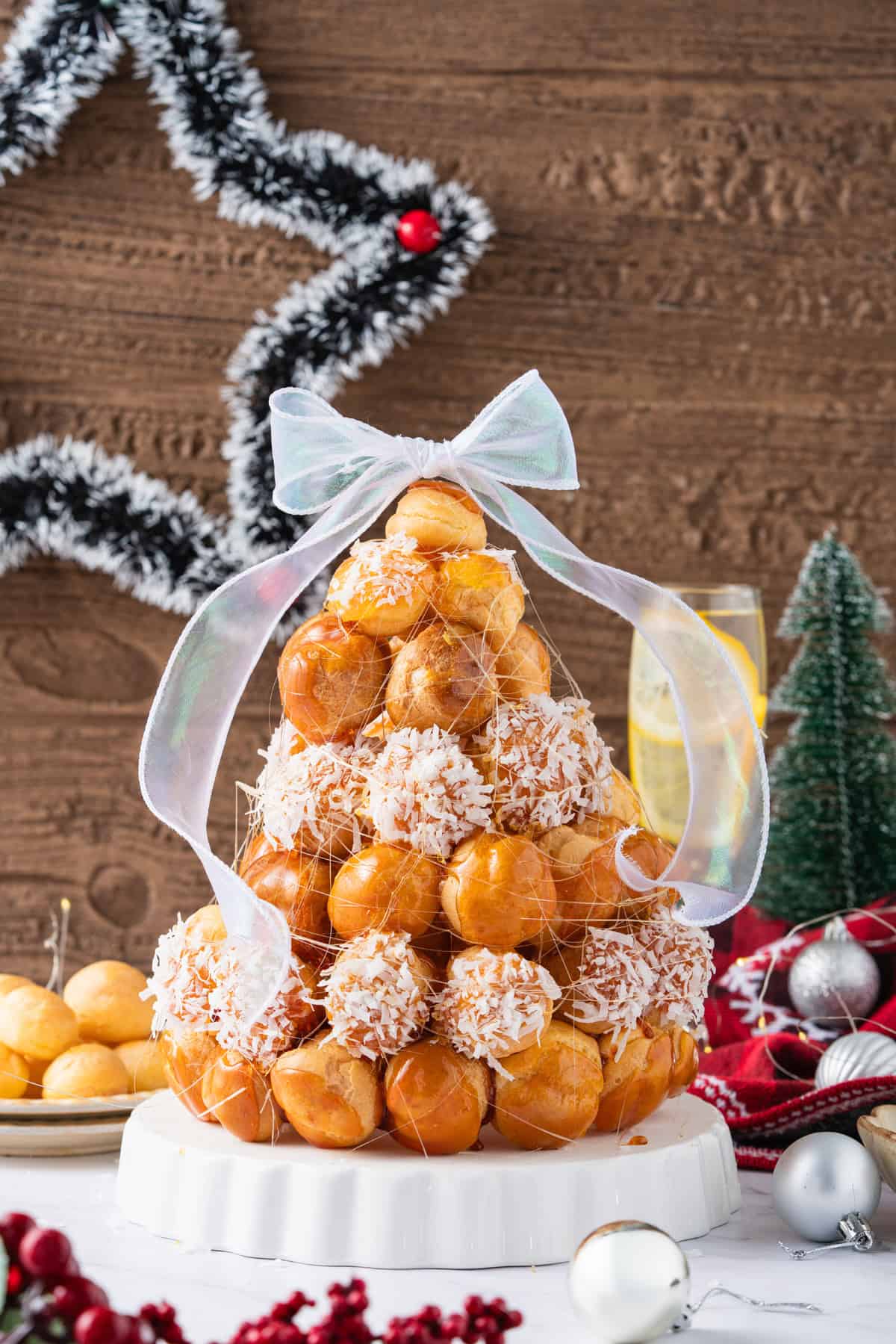 This festive Croquembouche features a stunning tower of cream puffs dipped in glossy amber caramel and sprinkled with shredded coconut. A festive Croquembouche tower with a bow