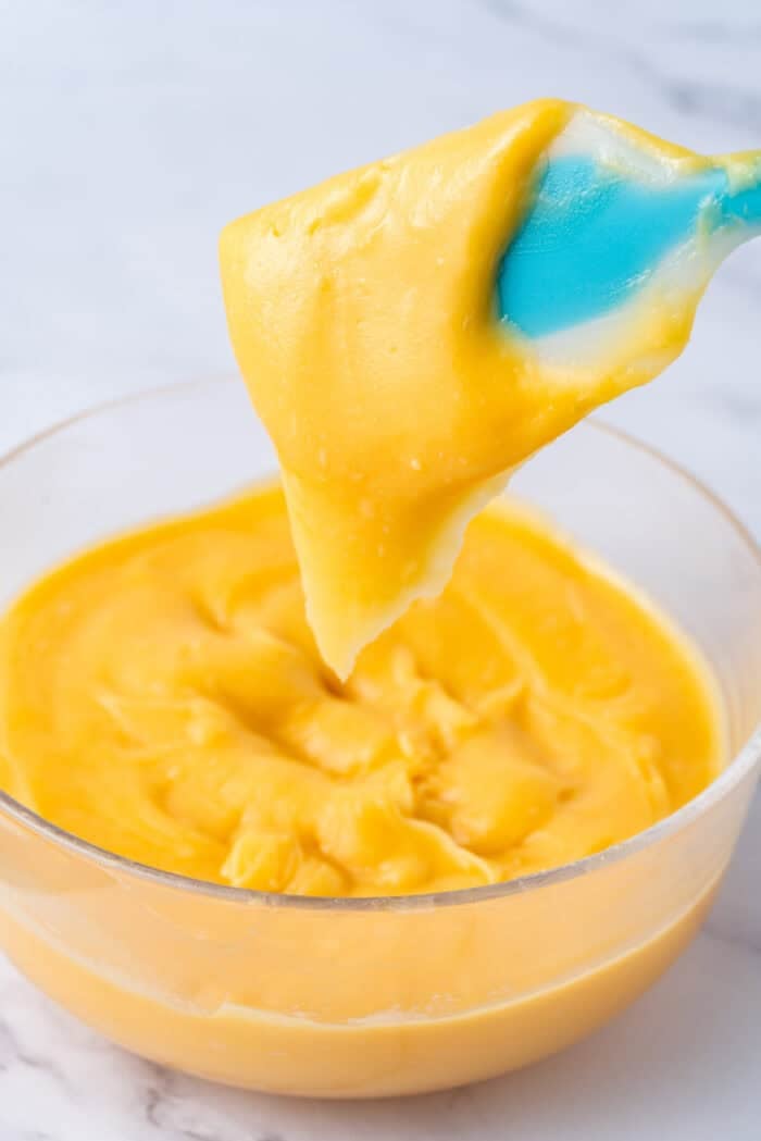 This festive Croquembouche features a stunning tower of cream puffs dipped in glossy amber caramel and sprinkled with shredded coconut. A spatula lifting choux pastry dough from the bowl