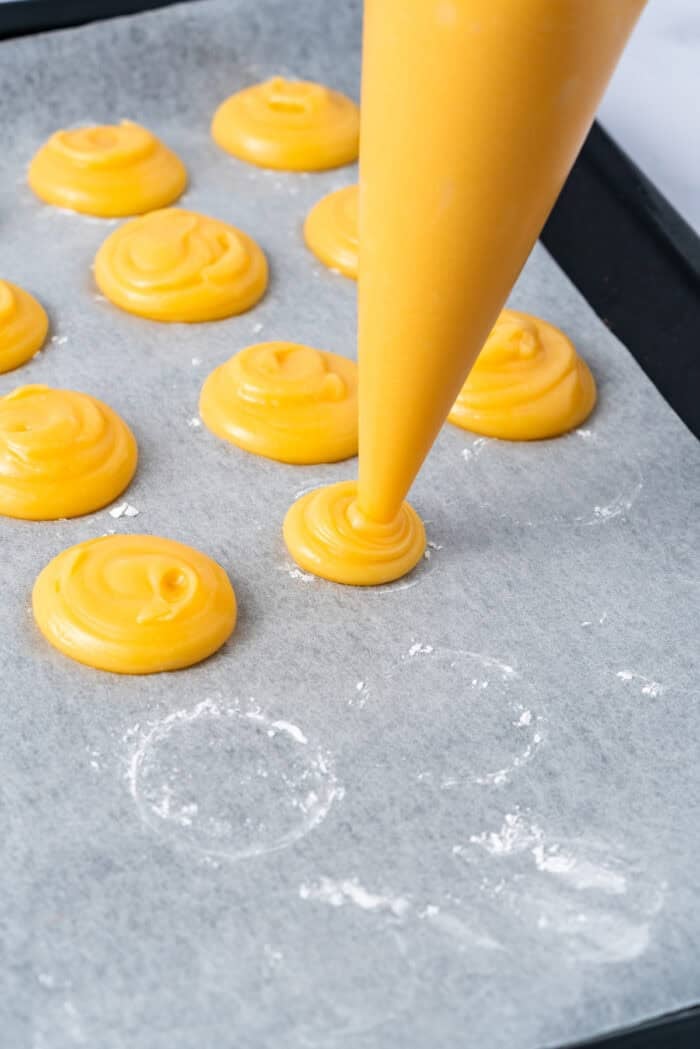 This festive Croquembouche features a stunning tower of cream puffs dipped in glossy amber caramel and sprinkled with shredded coconut. Piping choux pastry dough into circles
