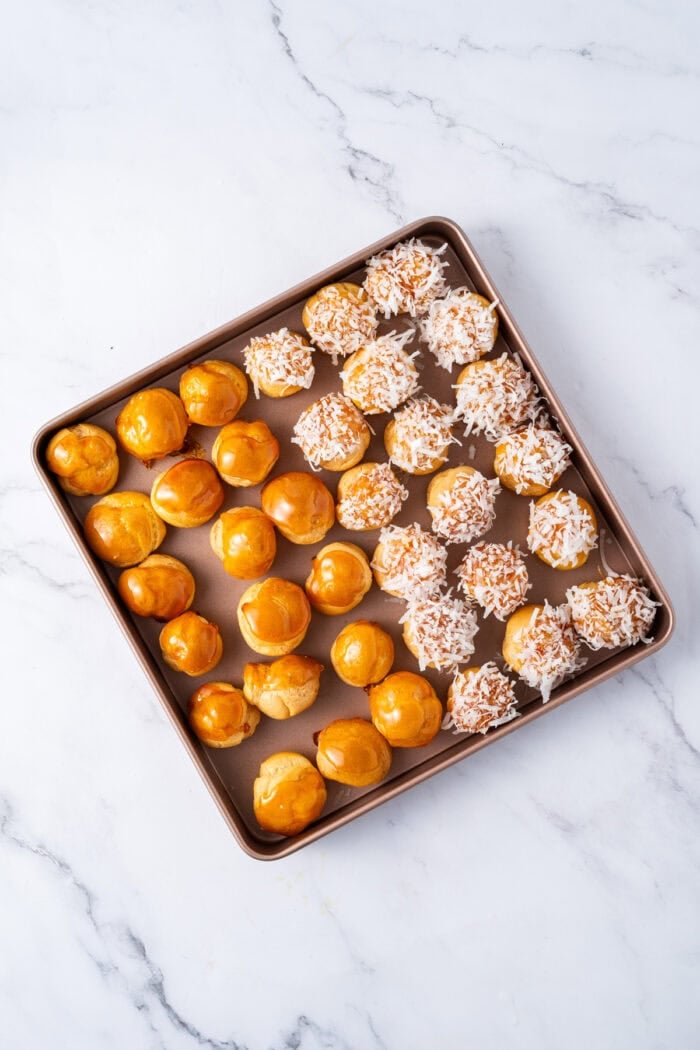 This festive Croquembouche features a stunning tower of cream puffs dipped in glossy amber caramel and sprinkled with shredded coconut. A tray of cream puffs dipped in caramel, half coated in coconut