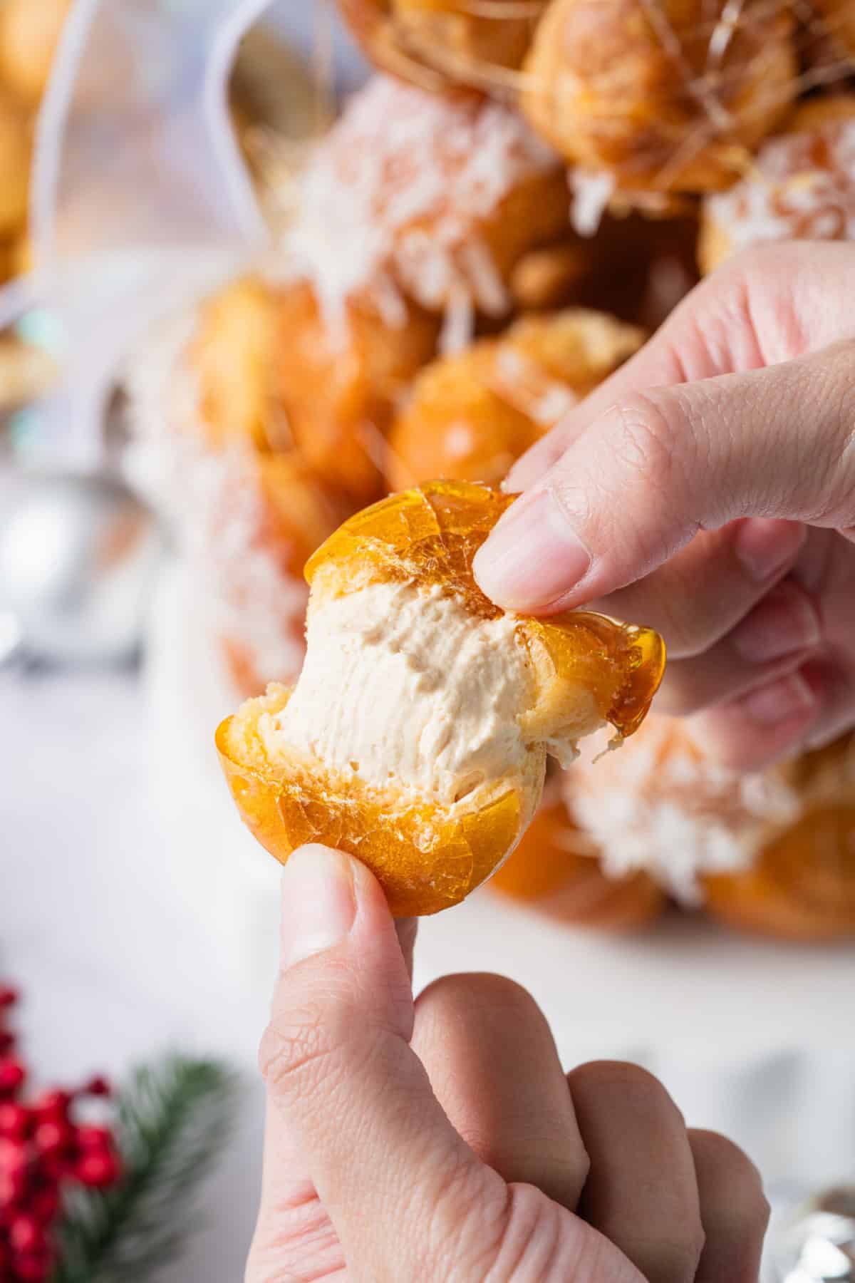 This festive Croquembouche features a stunning tower of cream puffs dipped in glossy amber caramel and sprinkled with shredded coconut. holding a Croquembouche cream puff