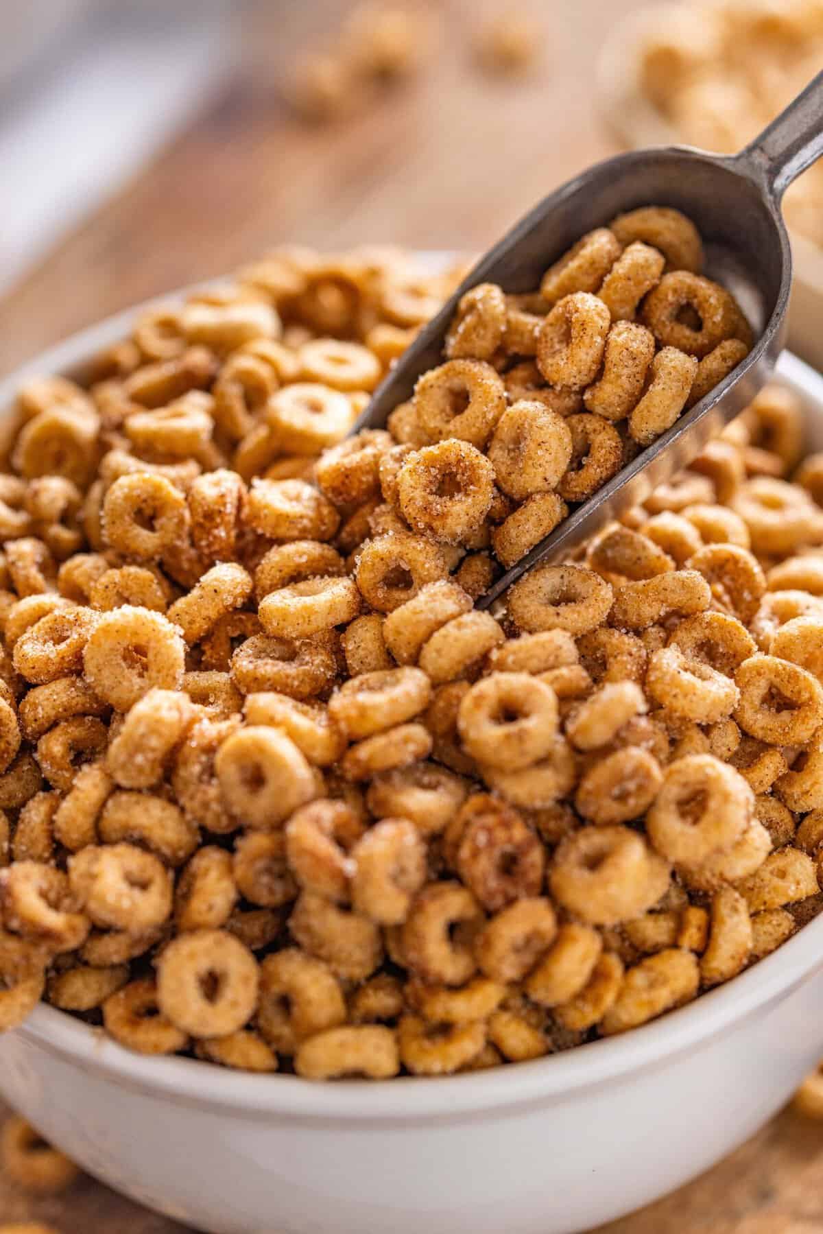 Hot Buttered Cheerios, aka Fried Cheerios, are a nostalgic snack featuring Cheerios toasted in butter and tossed with cinnamon sugar. A scooper in a bowl of hot buttered cheerios