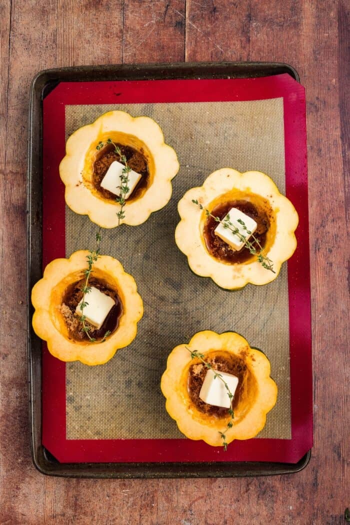 Squash is coated in a sweet, savory, and buttery glaze that caramelizes in the oven in this Maple Butter Roasted Acorn Squash recipe. Halved acorn squash filed with pats of butter and maple glaze