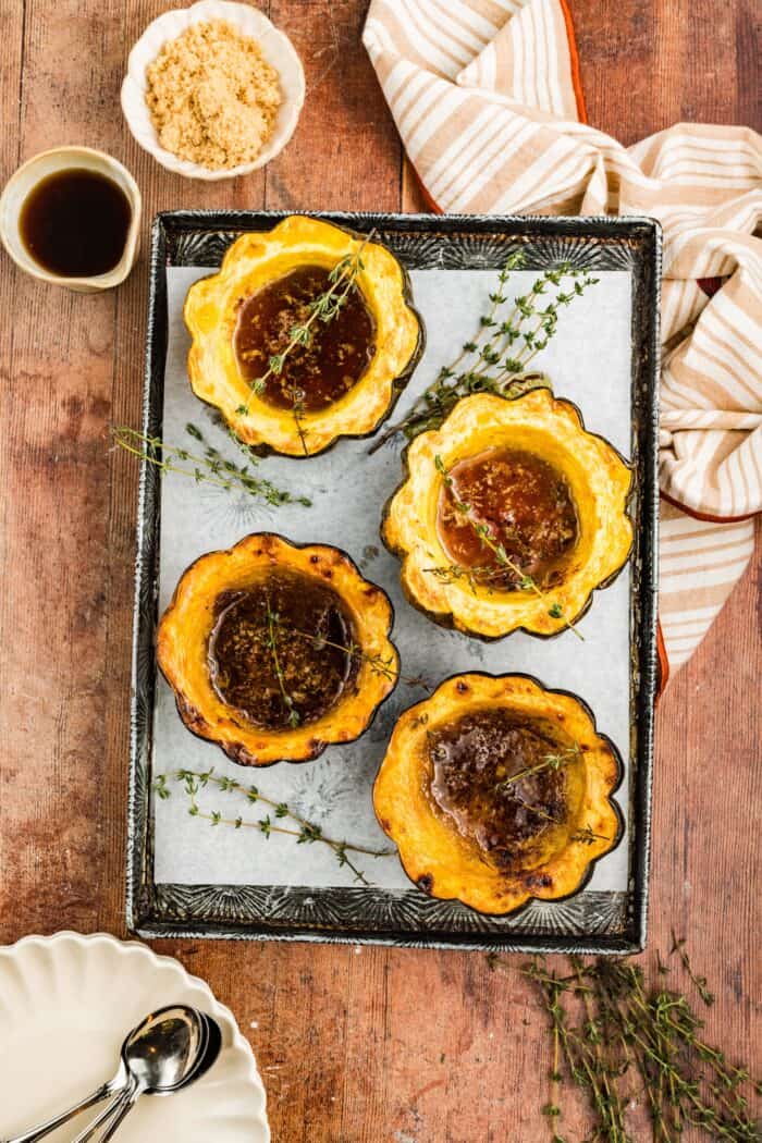 Squash is coated in a sweet, savory, and buttery glaze that caramelizes in the oven in this Maple Butter Roasted Acorn Squash recipe. Overhead view of maple butter roasted acorn squash halves