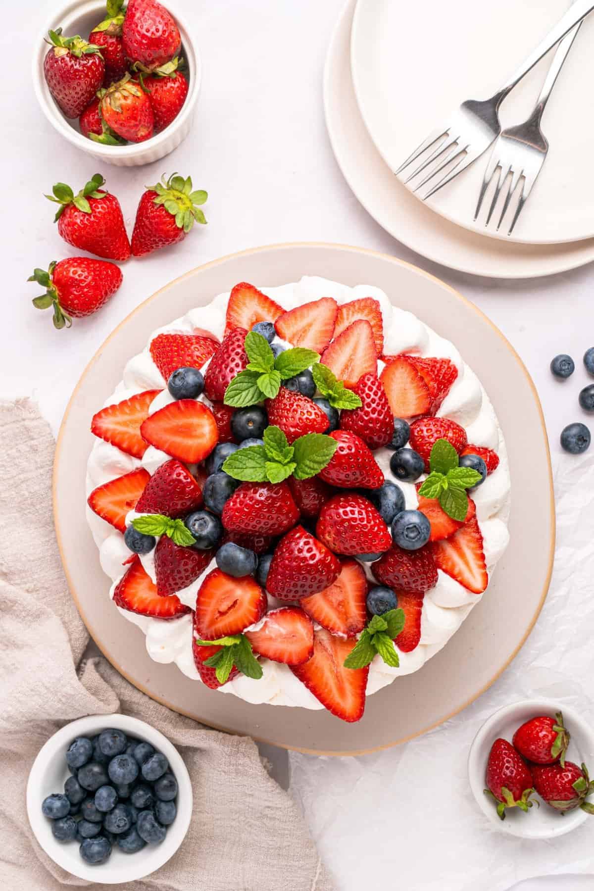 This Strawberry Meringue Cake is light, crisp, and creamy all at once with layers of meringue, fresh strawberries, and whipped cream. Overhead view of the top layer of strawberry meringue cake with strawberries, blueberries, and mint