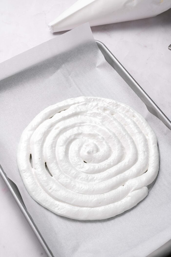 This Strawberry Meringue Cake is light, crisp, and creamy all at once with layers of meringue, fresh strawberries, and whipped cream. Meringue piped in a circle on a baking sheet