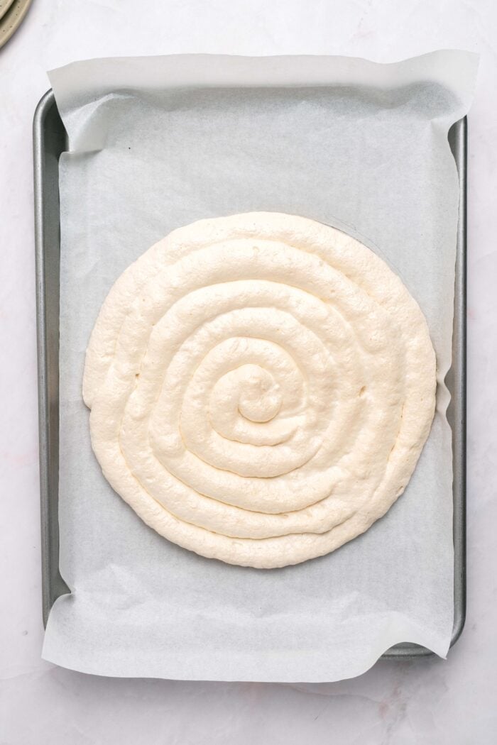 This Strawberry Meringue Cake is light, crisp, and creamy all at once with layers of meringue, fresh strawberries, and whipped cream. A circle of baked meringue on a baking sheet