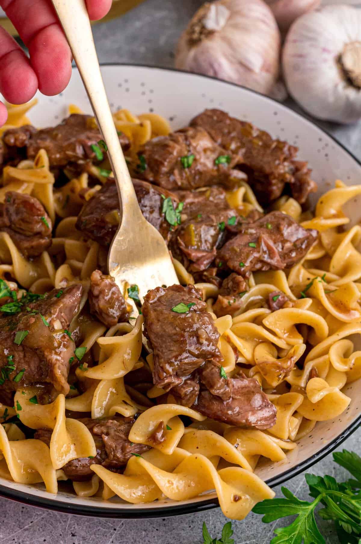 Tender chunks of beef are cooked in a rich, savory gravy and served over egg noodles in this easy Beef and Noodles recipe. A fork in a plate of beef and noodles