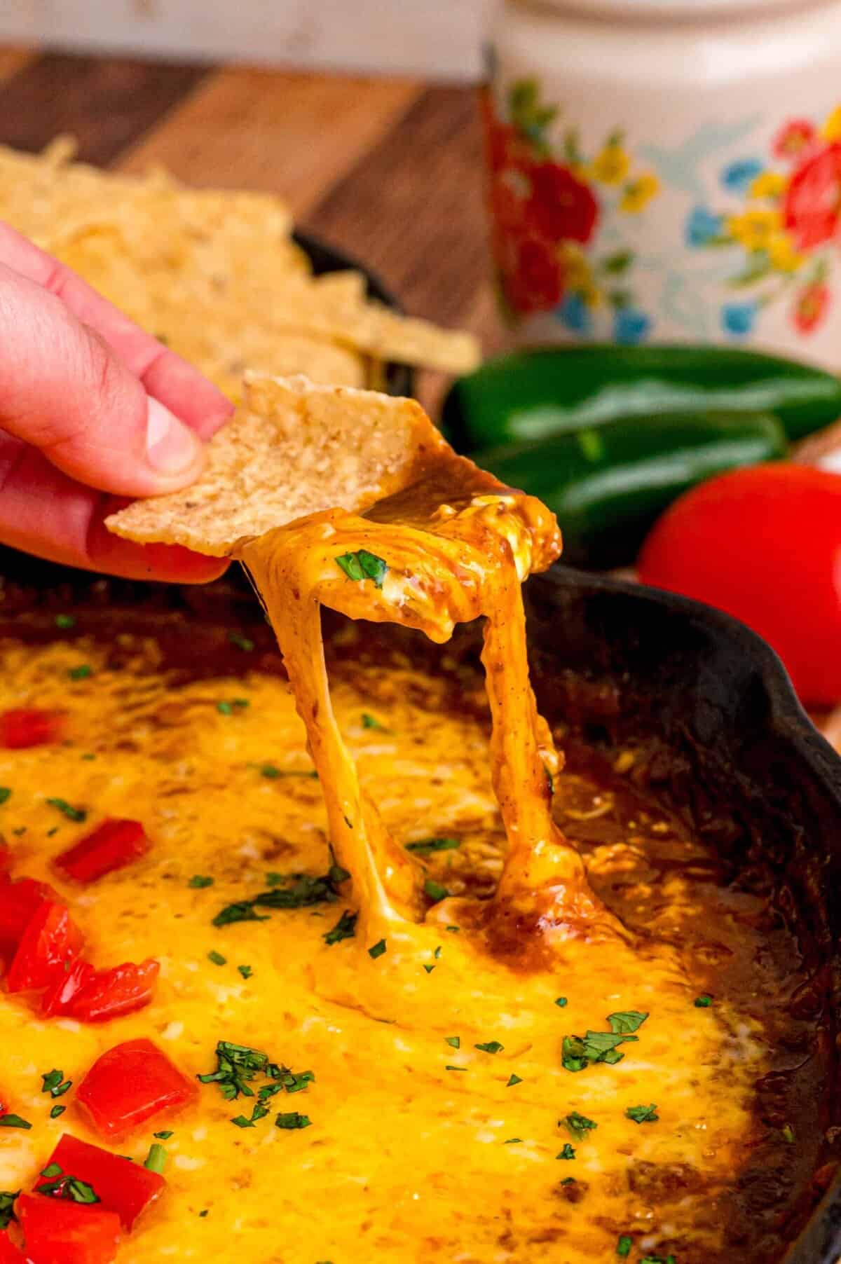 A hand dipping a tortilla chip in chili cheese dip