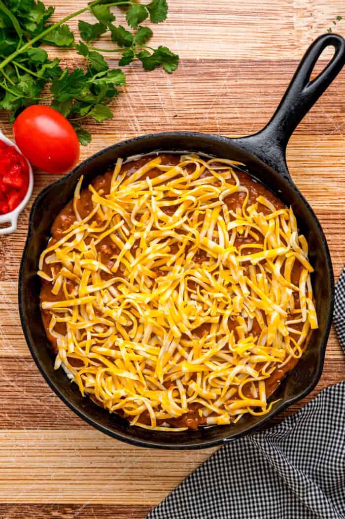 Cheese sprinkled on top of chili in a skillet