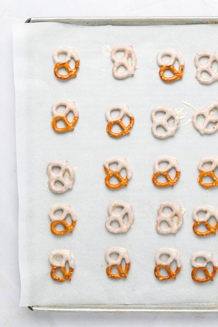These Chocolate Covered Pretzels are made with pretzel twists coated in dark and white chocolate and decorated with sprinkles. pretzels on a baking sheet dipped in white chocolate
