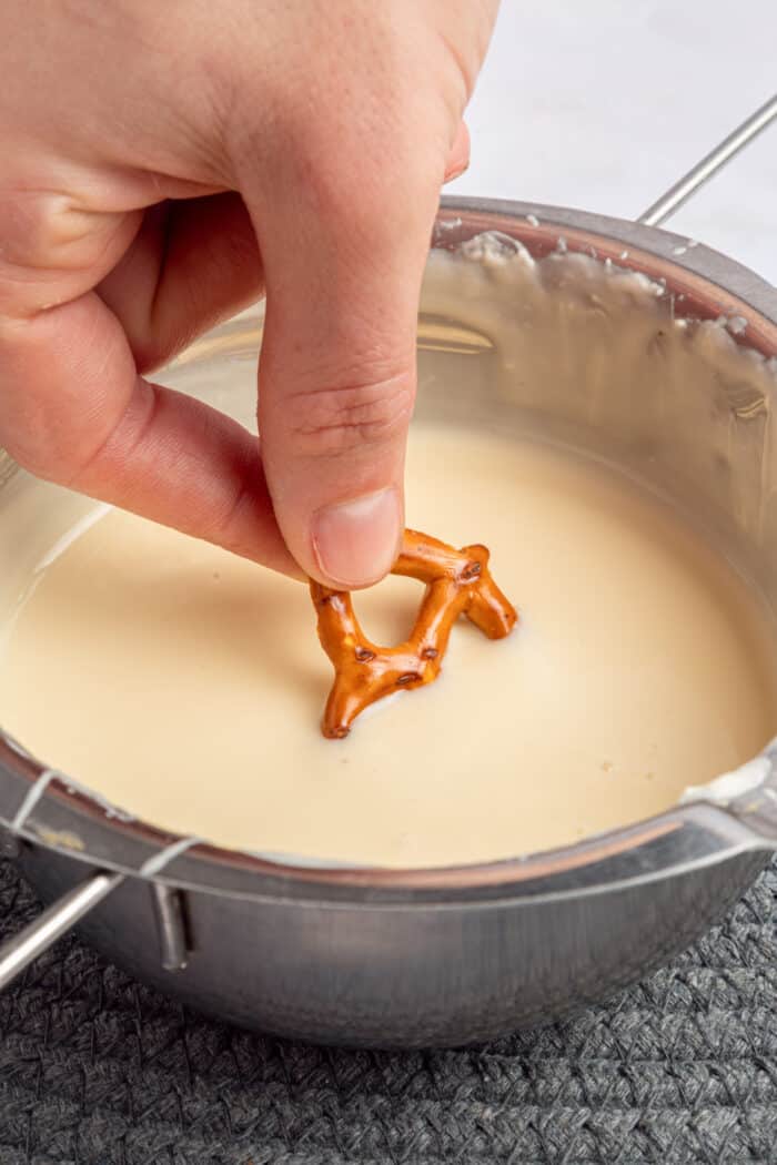 dipping a pretzel into melted white chocolate