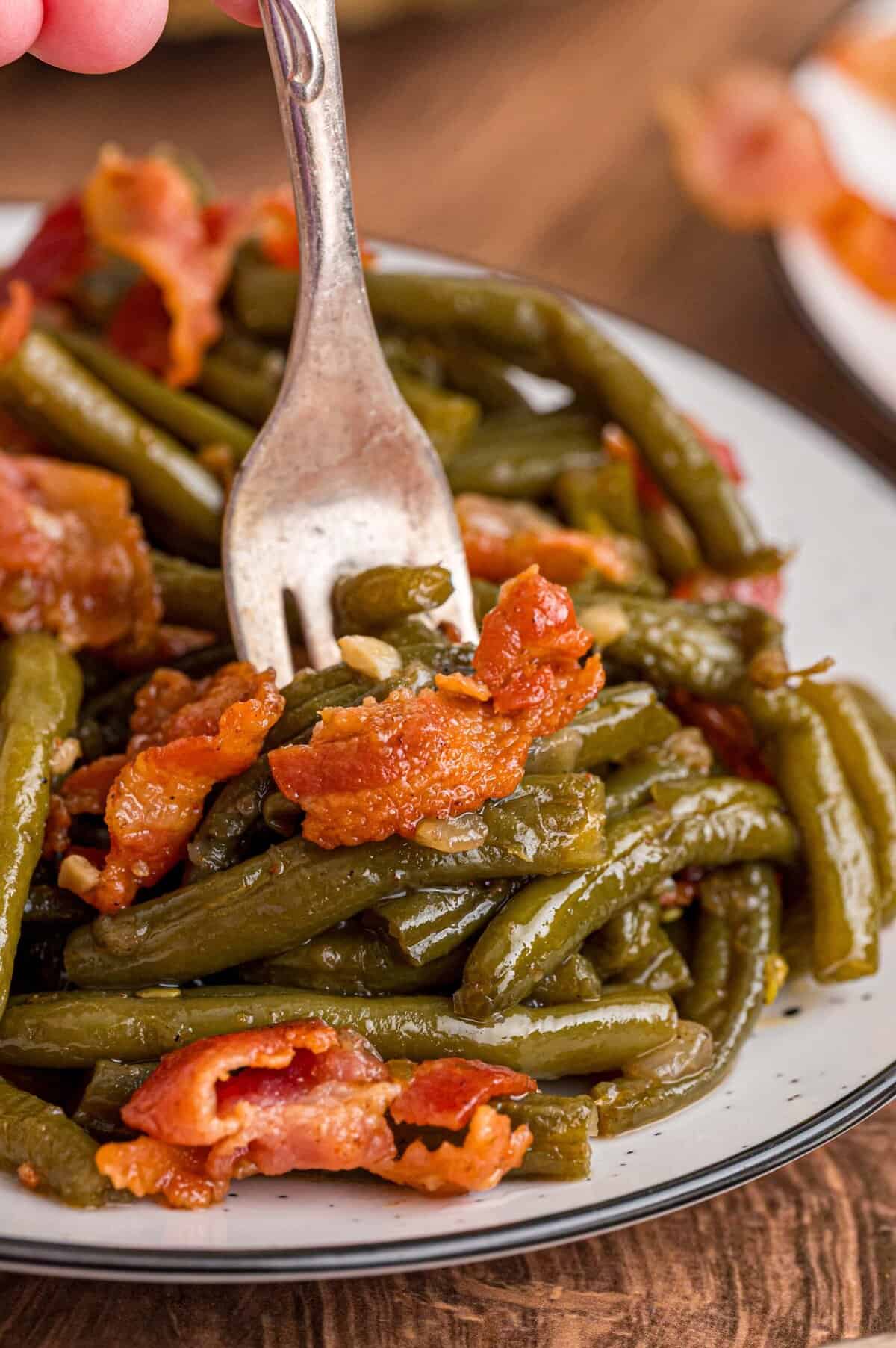 Fresh green beans are slow-cooked until tender with garlic, onion, bacon, and some Cajun seasoning in this Southern Green Beans recipe. A fork in a plate of Southern green beans