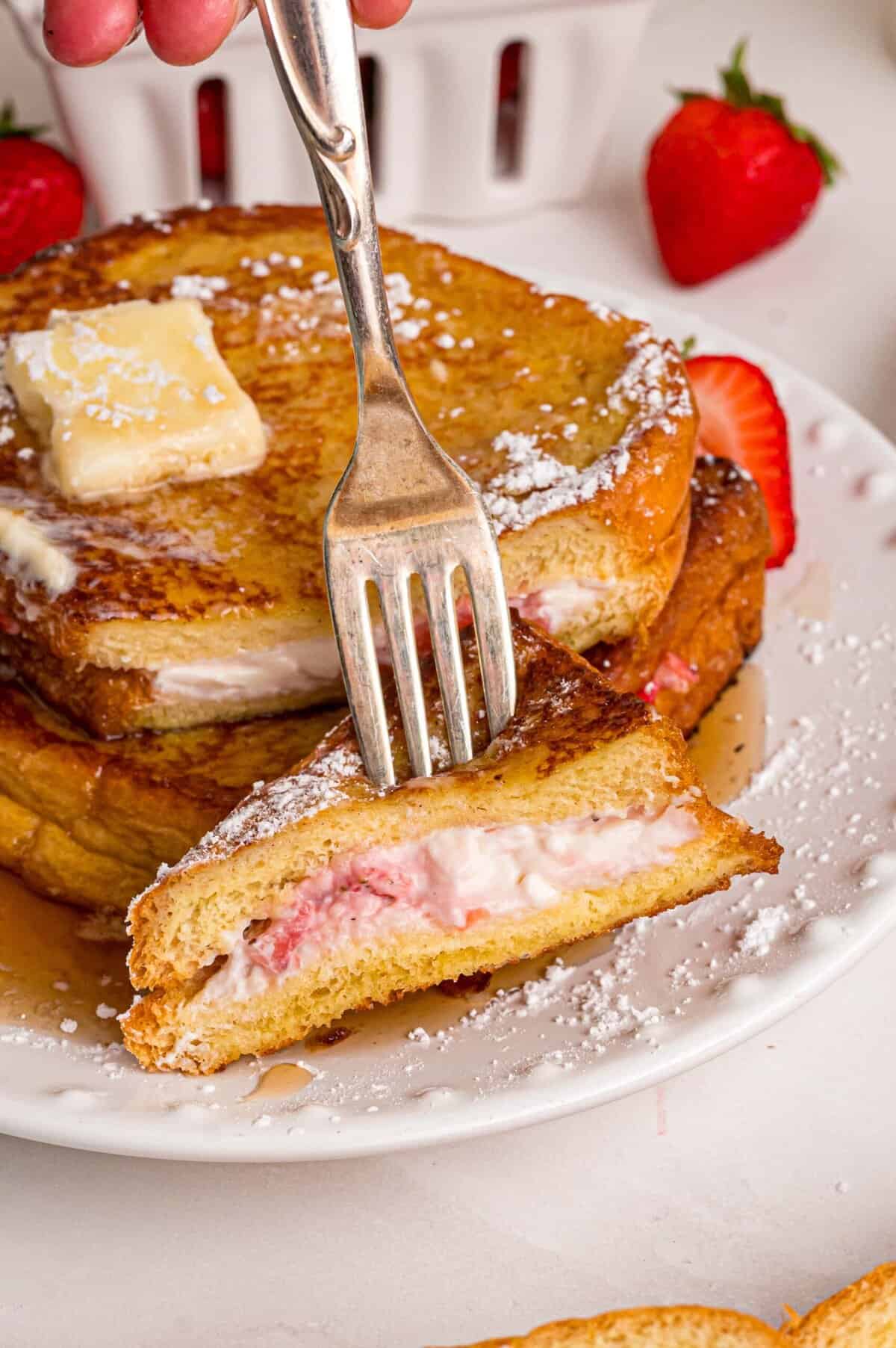 This Cream Cheese Stuffed French Toast recipe is an easy, decadent way to elevate basic French toast. Perfect for weekend brunch! A fork in a bite of stuffed French toast showing the cream cheese filling