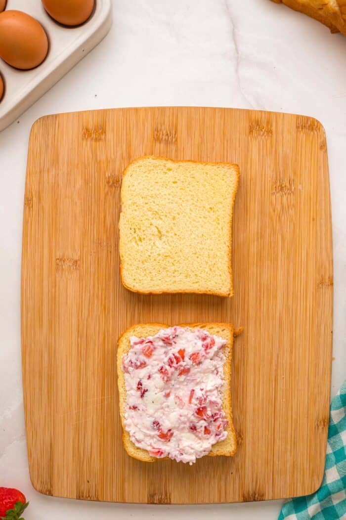 This Cream Cheese Stuffed French Toast recipe is an easy, decadent way to elevate basic French toast. Perfect for weekend brunch! A slice of Brioche topped with strawberry cream cheese and a plain slice on a cutting board