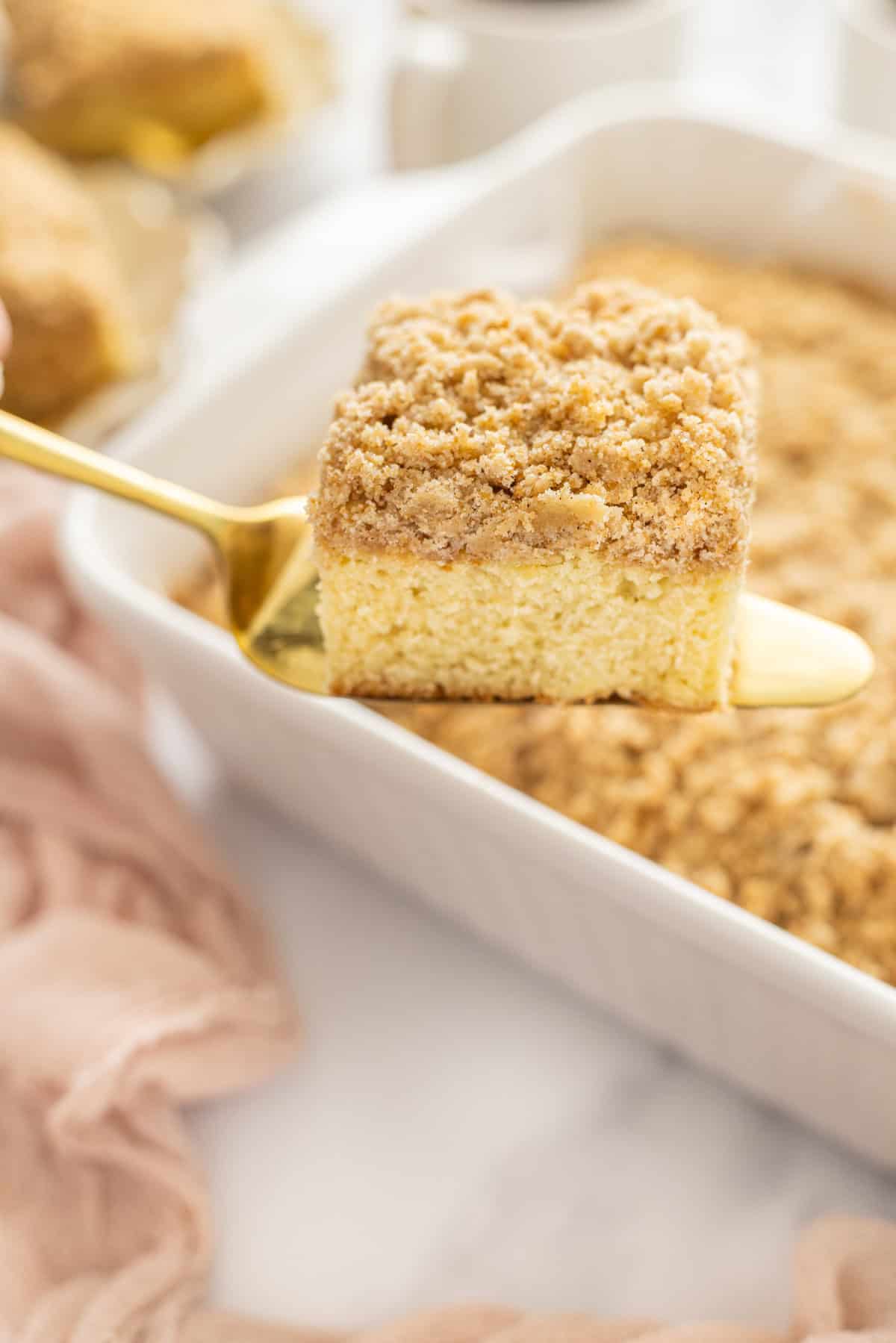 Tender, moist cake is topped with a thick layer of cinnamon crumb topping in this Easy Crumb Cake Recipe. Enjoy with a cup of coffee. Serving a slice of crumb cake