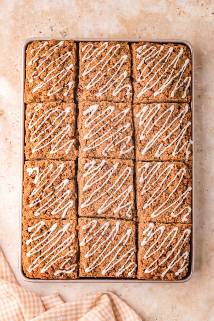 This Sour Cream Coffee Cake is soft and buttery with a generous cinnamon sugar ribbon baked through the middle & streusel topping. Overhead view of sour cream coffee cake drizzled with glaze