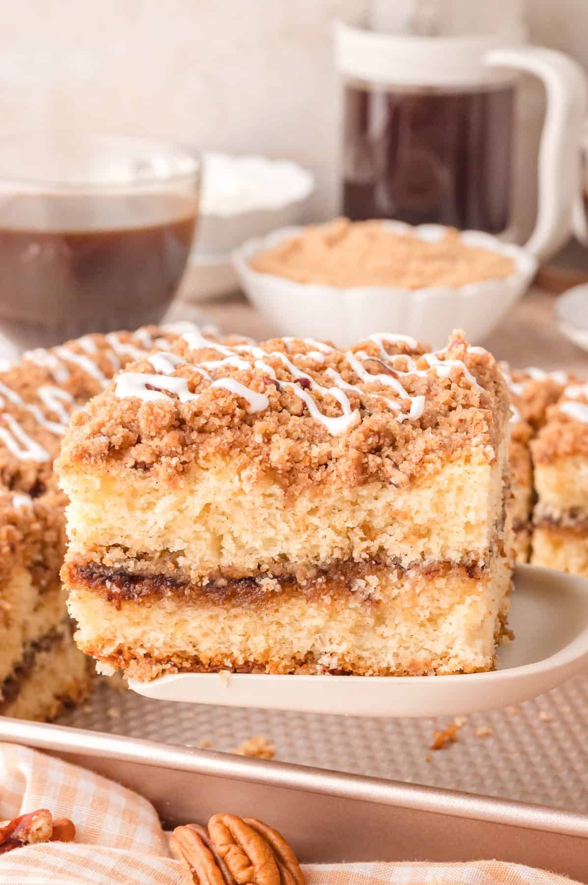 This Sour Cream Coffee Cake is soft and buttery with a generous cinnamon sugar ribbon baked through the middle & streusel topping. A slice of sour cream coffee cake on a white plate
