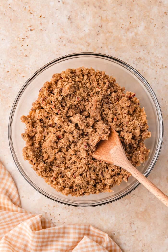 This Sour Cream Coffee Cake is soft and buttery with a generous cinnamon sugar ribbon baked through the middle & streusel topping. Stirring streusel ingredients with a wooden spoo