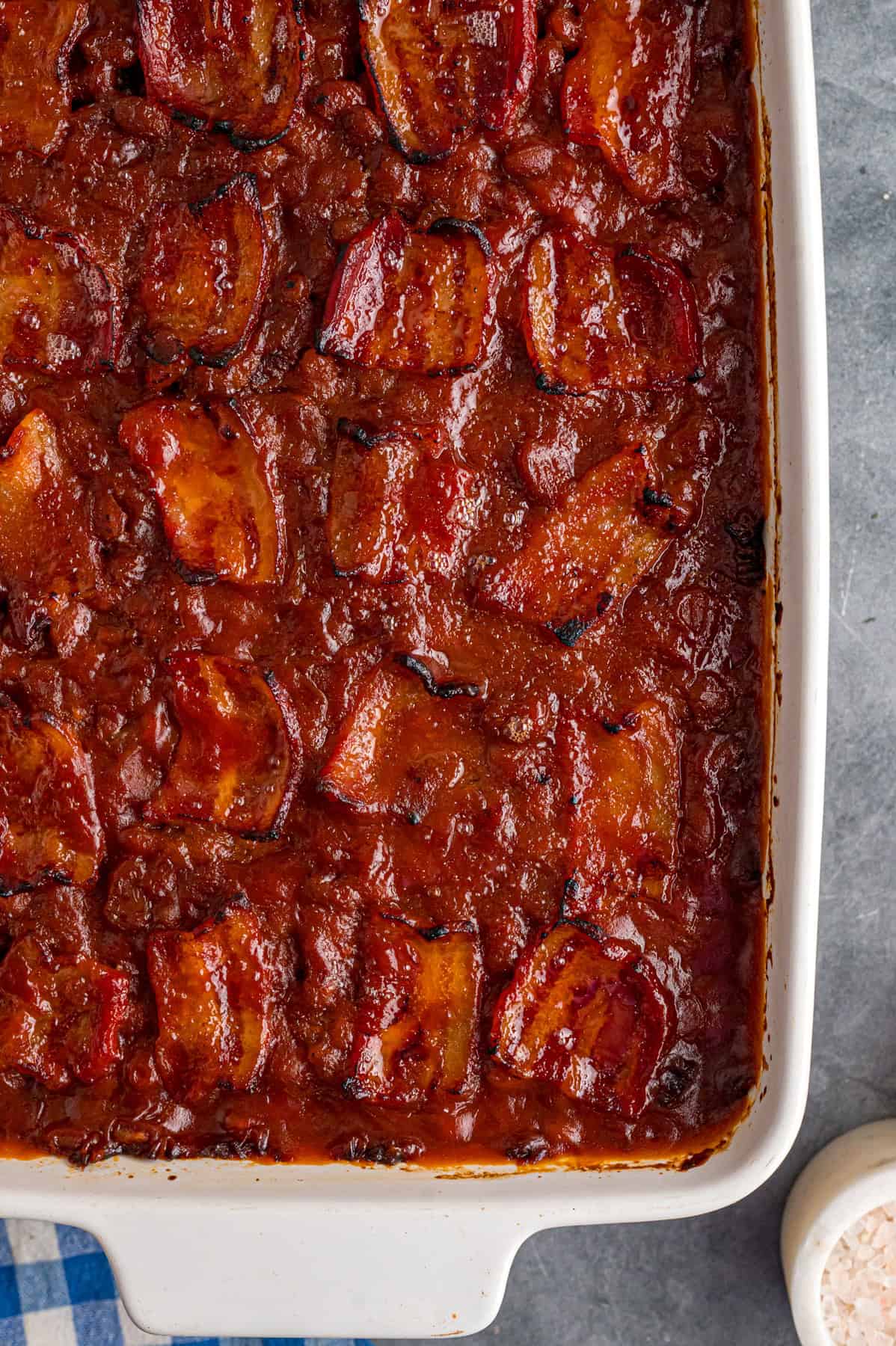 This easy Baked Beans recipe begins with pork and beans to keep things simple and salty bacon to add a final touch. Great for BBQs! Overhead view of a baking dish of homemade baked beans