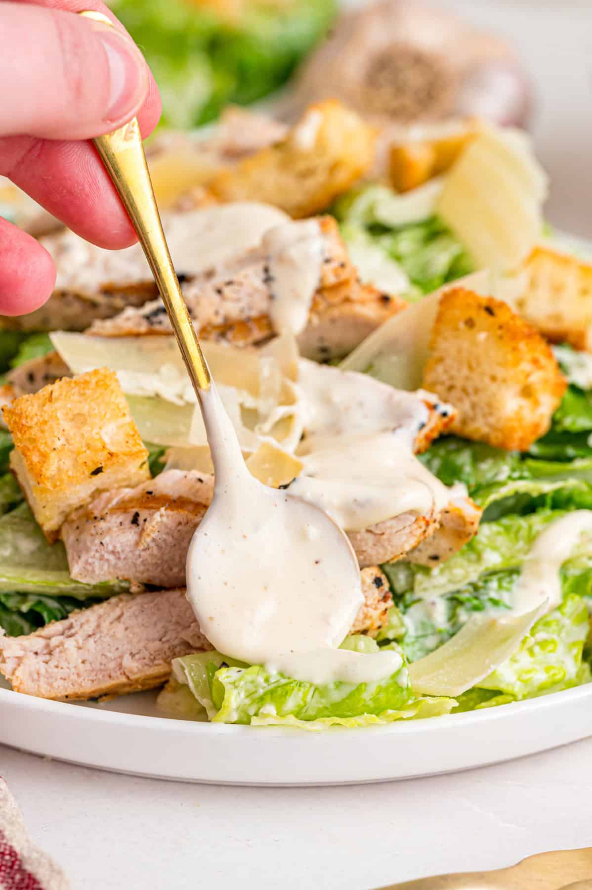 Crunchy seasoned croutons, creamy homemade dressing, and grilled strips of chicken make this Chicken Caesar Salad an easy dinner. Spooning caesar dressing over chicken caesar salad
