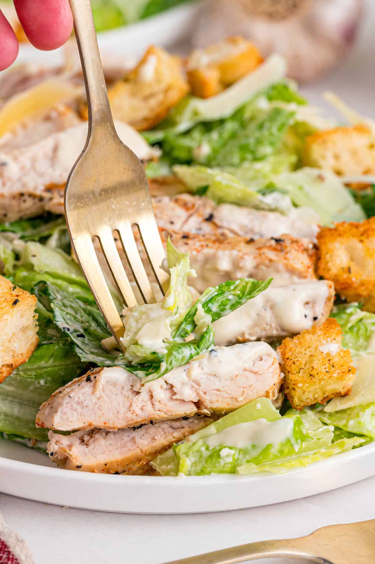 Crunchy seasoned croutons, creamy homemade dressing, and grilled strips of chicken make this Chicken Caesar Salad an easy dinner. A fork diving into a plate of chicken caesar salad