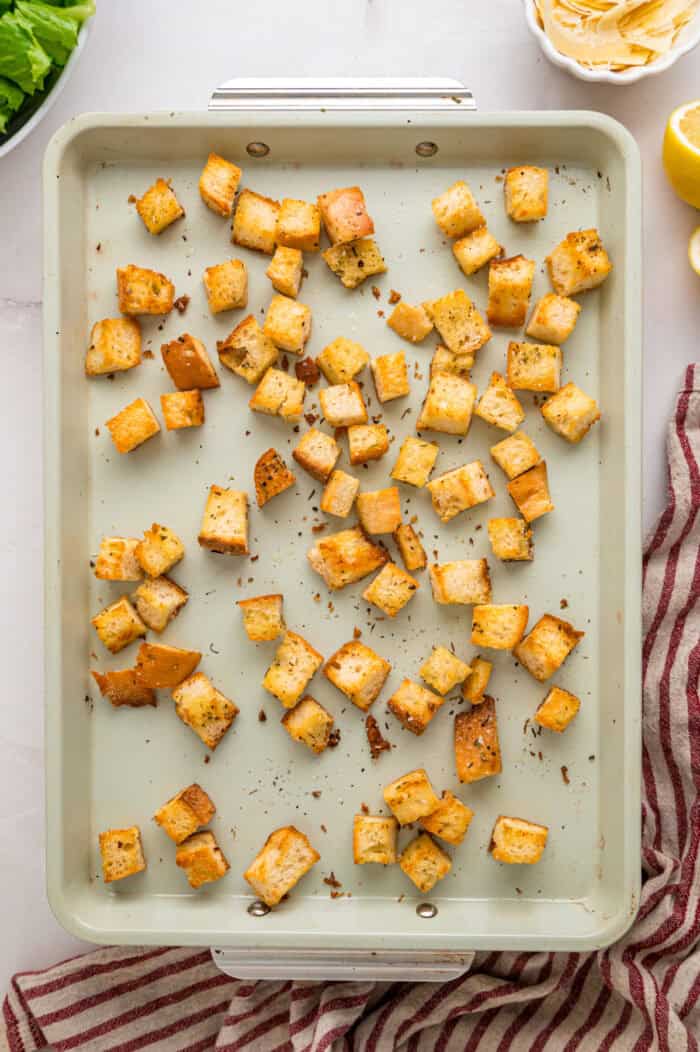 Crunchy seasoned croutons, creamy homemade dressing, and grilled strips of chicken make this Chicken Caesar Salad an easy dinner. Homemade croutons on a baking sheet