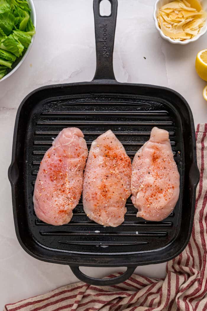Crunchy seasoned croutons, creamy homemade dressing, and grilled strips of chicken make this Chicken Caesar Salad an easy dinner. Three seasoned chicken cutlets on a grill pan