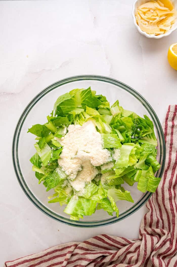 Crunchy seasoned croutons, creamy homemade dressing, and grilled strips of chicken make this Chicken Caesar Salad an easy dinner. Dollops of caesar dressing in a bowl of chopped romaine lettuce.