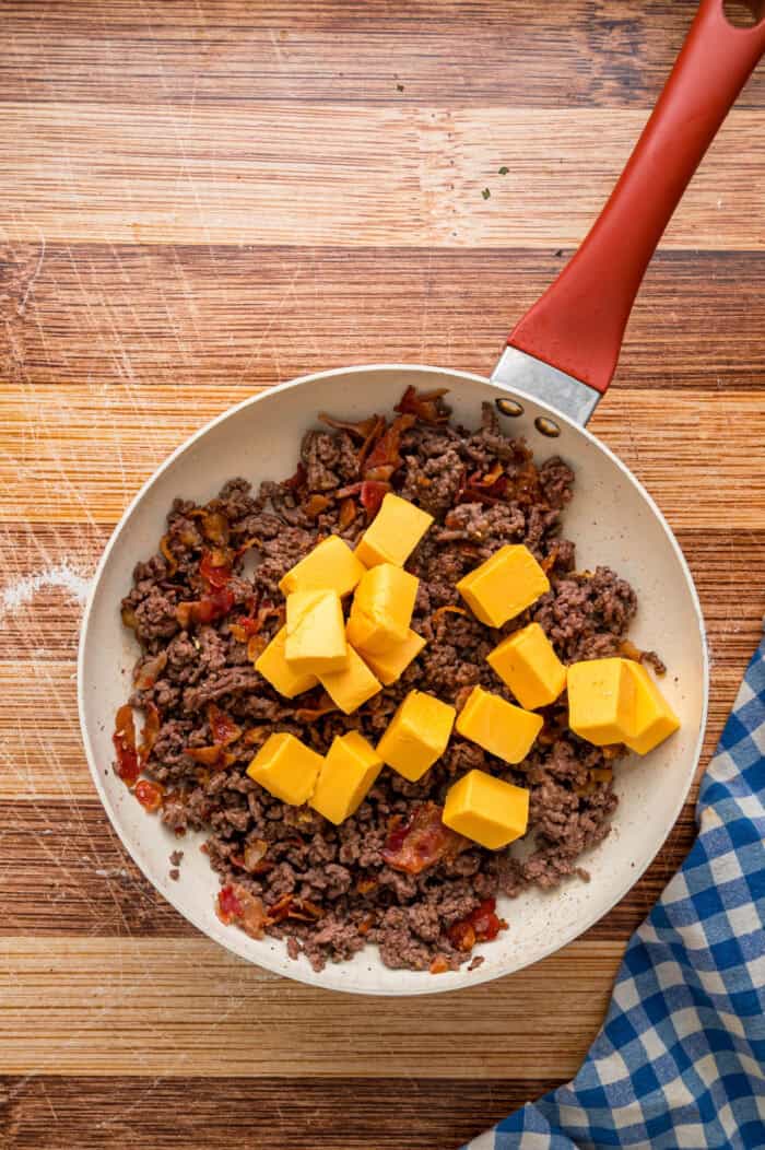 Ground beef, bacon, and cubes of Velveeta in a skillet