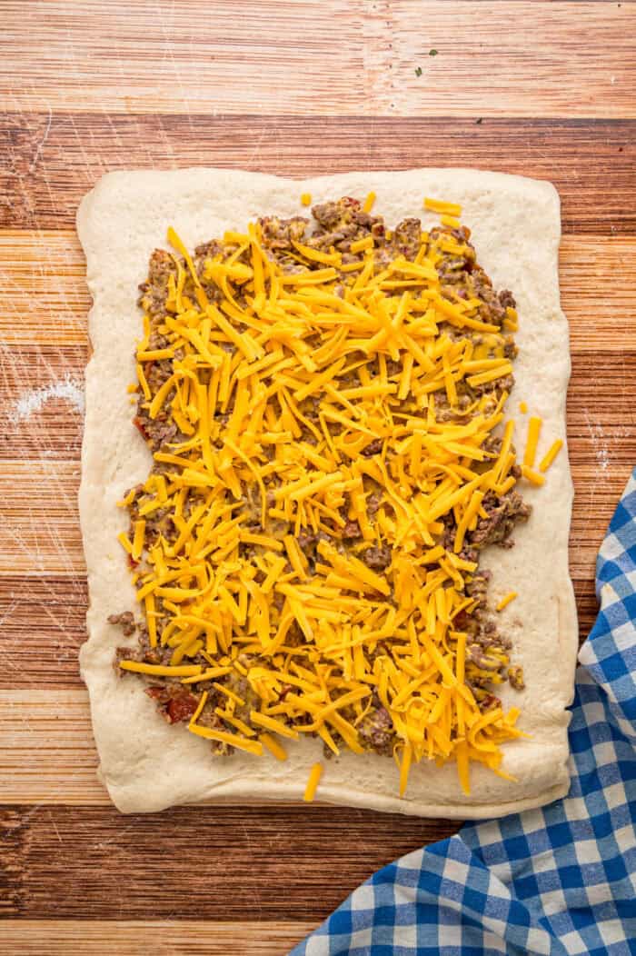 Ground beef mixture topped with shredded cheese on pizza dough