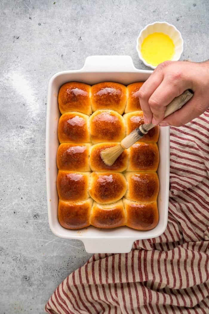 This Hawaiian Rolls recipe makes soft, fluffy rolls that taste just like the store-bought version – maybe even better. Brushing butter on Hawaiian rolls in a baking dish