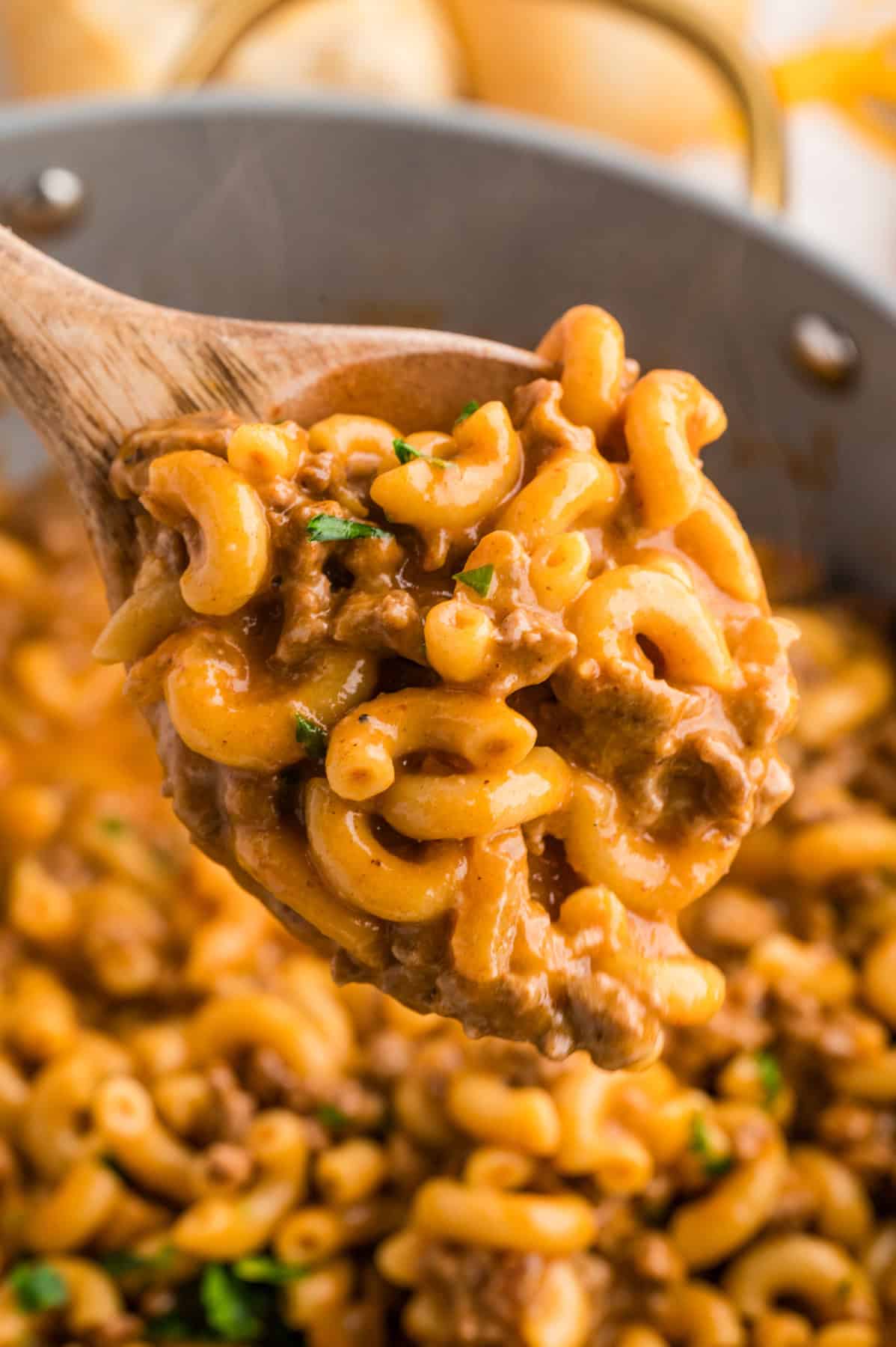 A wooden spoon of cheeseburger mac and cheese above the skillet