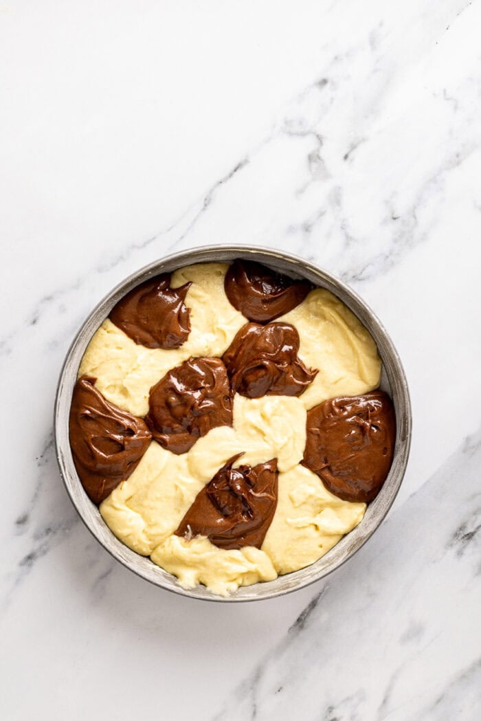 Chocolate and vanilla cake batter are swirled together, baked, and then layered with chocolate buttercream to create this Marble Cake recipe. Chocolate and vanilla cake in a checker pattern in a cake pan