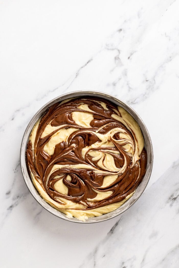 Chocolate and vanilla cake batter are swirled together, baked, and then layered with chocolate buttercream to create this Marble Cake recipe. Marble cake batter in a round pan