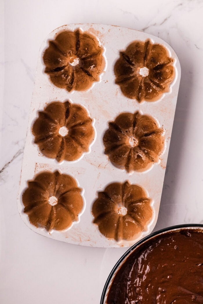 These Mini Chocolate Bundt Cakes offer a rich chocolate flavor and ultra-moist crumb in perfectly portioned, individual cakes. A mini bundt cake pan coated with butter and cocoa powder
