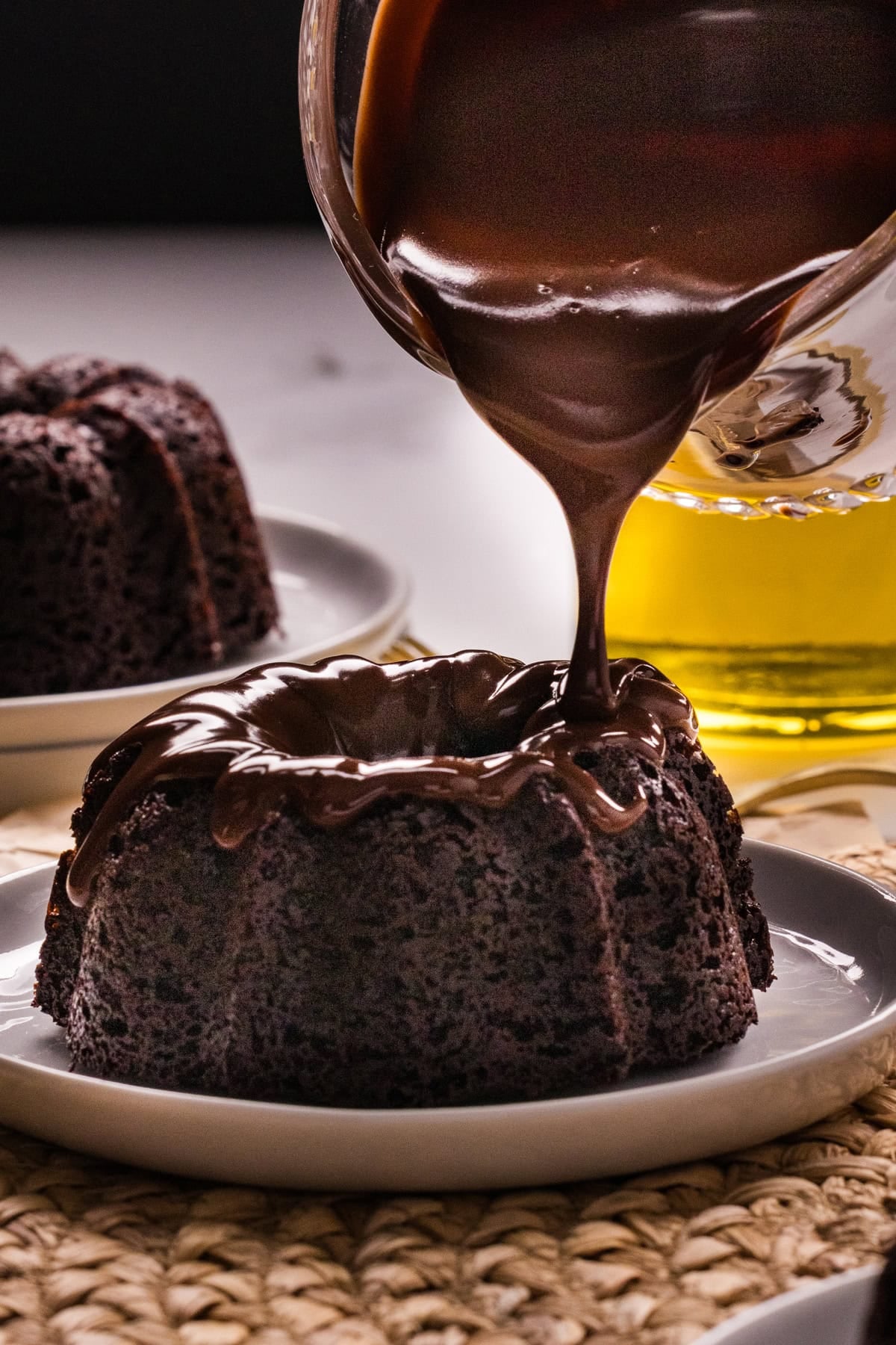 These Mini Chocolate Bundt Cakes offer a rich chocolate flavor and ultra-moist crumb in perfectly portioned, individual cakes. Drizzling chocolate ganache over a mini chocolate bundt cake on a white plate